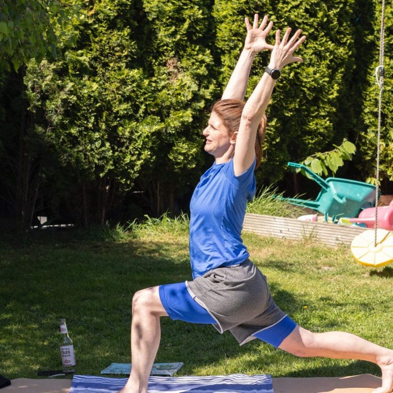Yoga im Garten - Yoga-Lehrerin in einer Yoga-Pose Person in blauer Sportkleidung macht einen Krieger-II-Yoga-Pose im Freien.