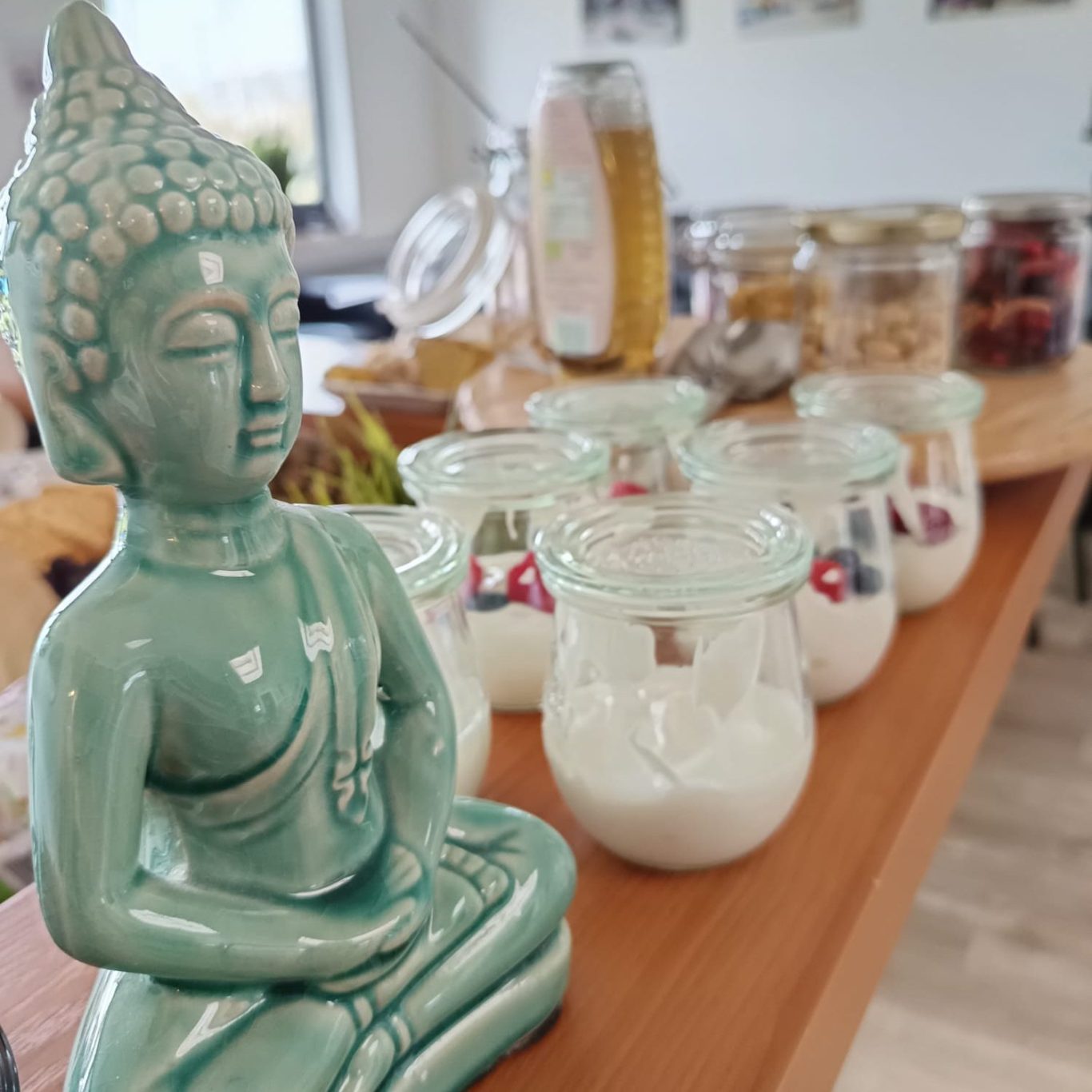 Grüne Buddha-Statue neben Glasbehältern mit Joghurt und einem Frühstückstisch.