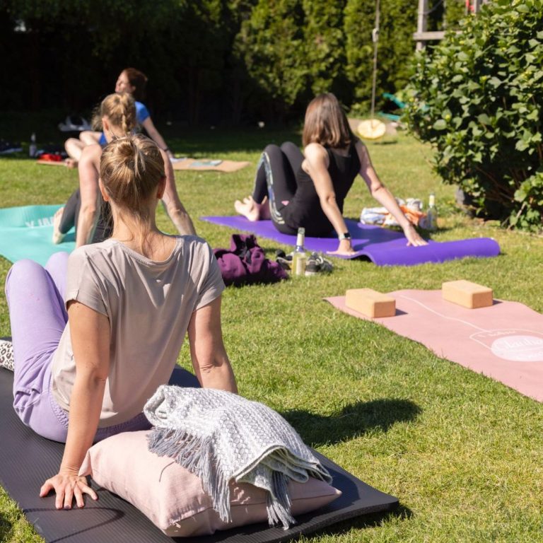Gruppensitzung im Freien mit Frauen, die Yoga auf Matten im Gras praktizieren.